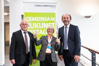 2 lächelnde Männer außen und eine lächelnde Frau mit Daumen hoch in der Mitte